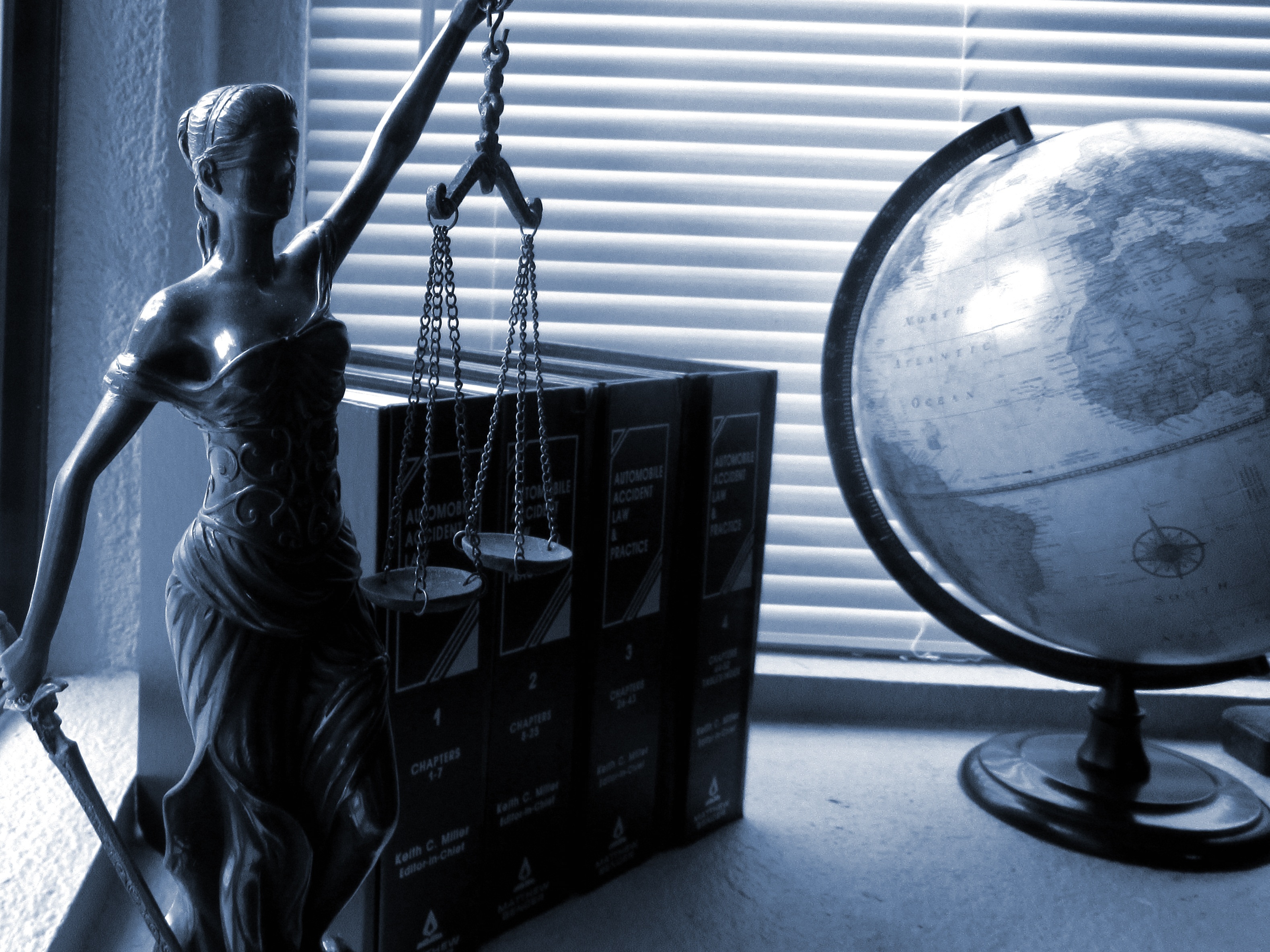 A sculpture of a blindfolded lady justice with a sword and scales. Behind it are books and a globe.