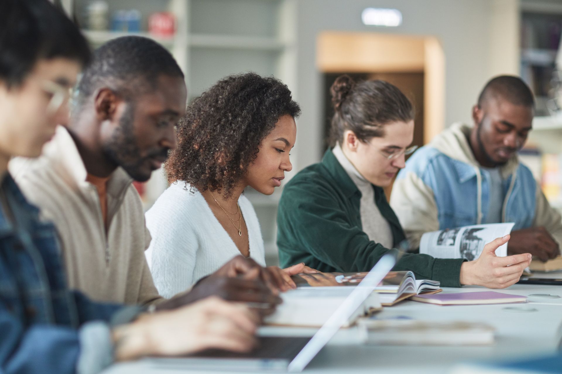 Multiracial group of college students studying together indoors in a library.
